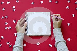 Notebook with female hands on Red Christmas background with snowflakes.
