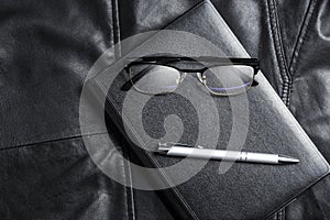 Notebook, glasses and pix over black leather background