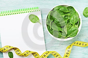 Notebook, green spinach leaves and tape measure on wooden table top view. Diet and healthy food.