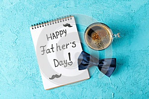 Notebook with inscription happy fathers day, blue bow tie and cup of coffee on color background, space for text