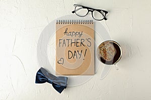 Notebook with inscription happy fathers day, blue bow tie, cup of coffee and glasses on white background