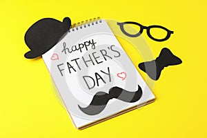 Notebook with inscription happy fathers day, decorative bow tie, glasses, mustache and hat on color background