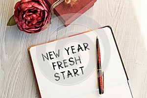 Notebook with inscription NEW YEAR FRESH START on a light table along with a flower and a vintage gift box. Natural light. View