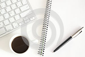 Notebook and keyboard next to a cup of coffee on a white desktop. Home working concept