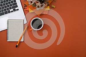 Notebook, laptop computer and coffee cup on orange background with copy space.