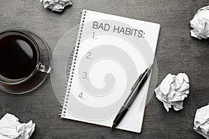 Notebook with list of bad habits, pen, crumpled paper balls and cup of coffee on grey table, flat lay. Change your lifestyle