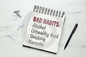 Notebook with list of bad habits and pen on white marble table, flat lay. Change your lifestyle