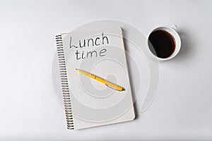 Notebook with LUNCH TIME inscription. Cup of coffee and pen white background. Top view