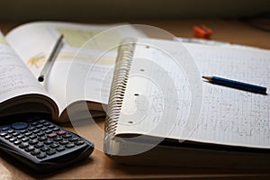 A notebook with math exercises written in pencil next to a calculator