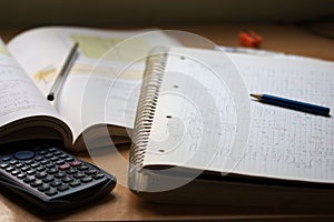 A notebook with math exercises written in pencil next to a calculator photo