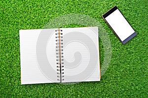 Notebook and mobile phone on green grass.