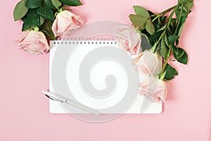 Notebook mock up and pink roses top view on pink background. Flat lay. Copy space.