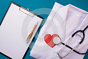 A notebook for notes, the folded form of a doctor lies on the table, a red heart and a stethoscope lies nearby