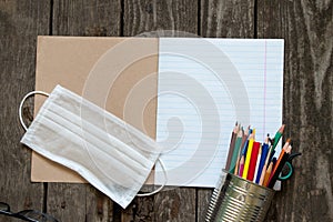 Notebook open in a ruler colored pencils and a medical mask on the school desk, home education