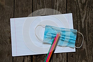 Notebook open in a ruler colored pencils and a medical mask on the school desk, home education