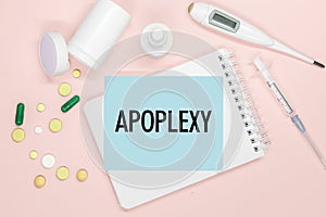 Notebook page with text APOPLEXY on a table, pills and syringe. Medical concept photo