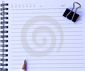 Notebook paper with white pencil and black paper clip on white background for texture