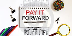 Notebook with PAY IT FORWARD word with office tools on white table