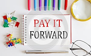 Notebook with PAY IT FORWARD word with office tools on the white table