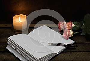 Notebook, pen, candle roses on dark background