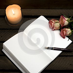 Notebook, pen, candle roses on dark background