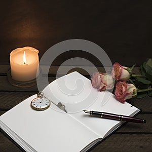 Notebook, pen, candle roses on dark background