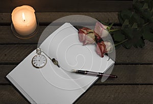 Notebook, pen, candle roses on dark background