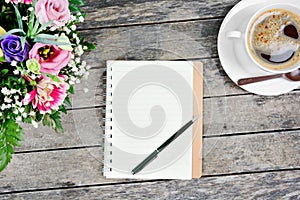 Notebook with pen, coffee cup and colorful flowers on table