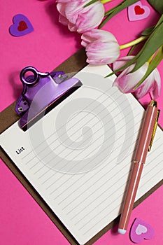 Notebook with pen, cup of coffee, tulip spring flower and cute hearts on pink background, flat lay