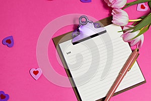 Notebook with pen, cup of coffee, tulip spring flower and cute hearts on pink background, flat lay