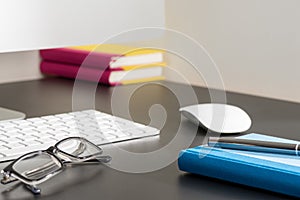 Notebook, Pen, and Eyeglasses Alongside Computer on Office Desk