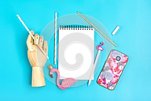 Notebook, pen, flamingo figure, smartphone, wooden hand hold drinking paper straws on blue background