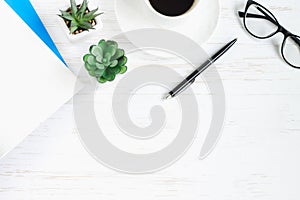 Notebook, pen, glasses, plants succulents, a cup of coffee on a white wooden table, flat lay, top view. Office table desk,