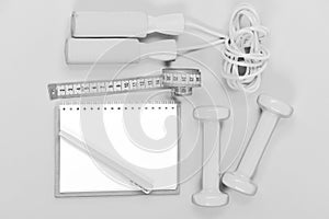 Notebook, pen and gym equipment top view on yellow background. Weight loss and active lifestyle concept. Blocknote, pen