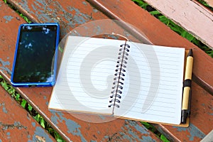 Notebook with pen and mobile phone on the brown bench