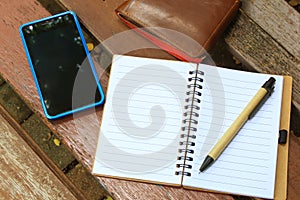 Notebook with pen, mobile phone and wallet on the brown bench