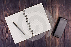 Notebook with pen on wooden table with a phone