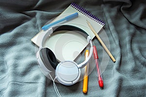 A notebook with pencil, colorful felt-tip pens and headphones on a gray plaid background. Cosy workspace. Top view