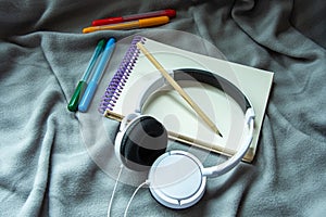 A notebook with pencil, colorful felt-tip pens and headphones on a gray plaid background. Cosy workspace. Top view