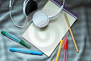 A notebook with pencil, colorful felt-tip pens and headphones on a gray plaid background. Cosy workspace. Top view, flat lay