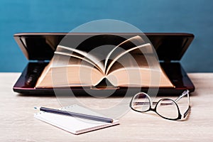 Notebook, pencil and glasses on a background of a book in an open laptop table. Distance learning.