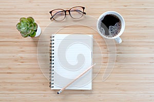 Notebook with pencil , glasses, small tree and coffee on old wooden table.Top view