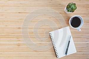 Notebook with pencil , glasses, small tree and coffee on old wooden table.Top view