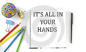 Notebook ,pencils,pen and rubber band with text IT`S ALL IN YOUR HANDS on the white background