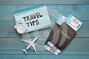 Notebook with phrase Travel Tips and tourist items on light blue wooden table, flat lay