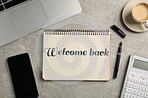 Notebook with phrase Welcome Back on grey table. Office desk with laptop and coffee, flat lay photo