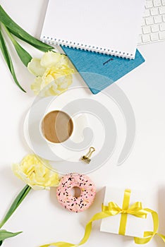 Notebook for daily planning with breakfast serving on a white background, a cup of coffee, a donut, flowers and a gift box with a