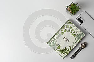 A notebook, a plant, a smartphone and a wristwatch on a light background