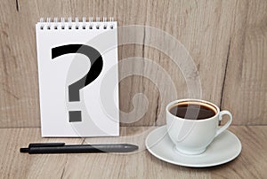 Notebook with question mark  coffee and black pen  light colored wooden background