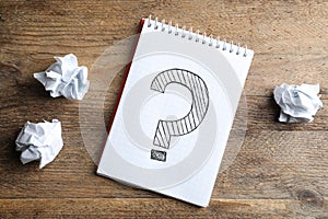 Notebook with question mark and crumpled paper on wooden table